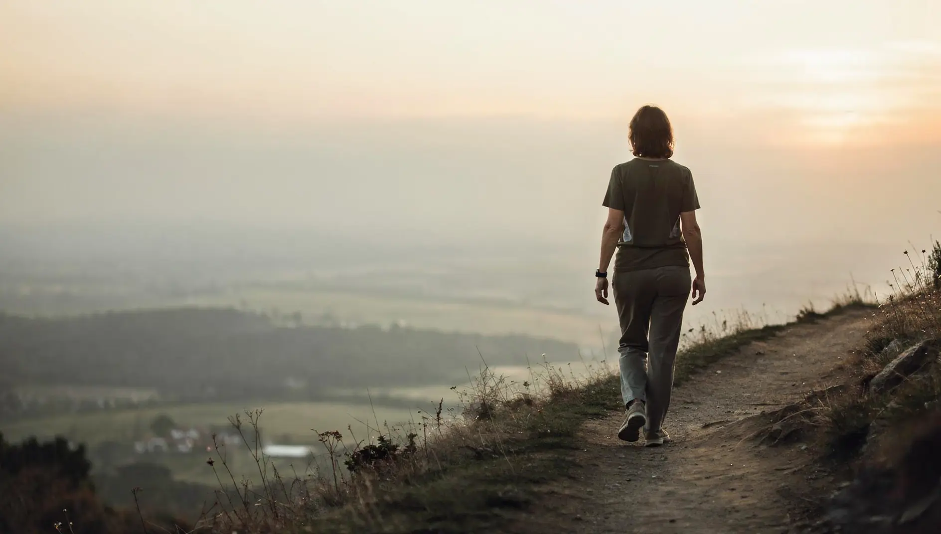A person walking a hillside trail toward the sunrise